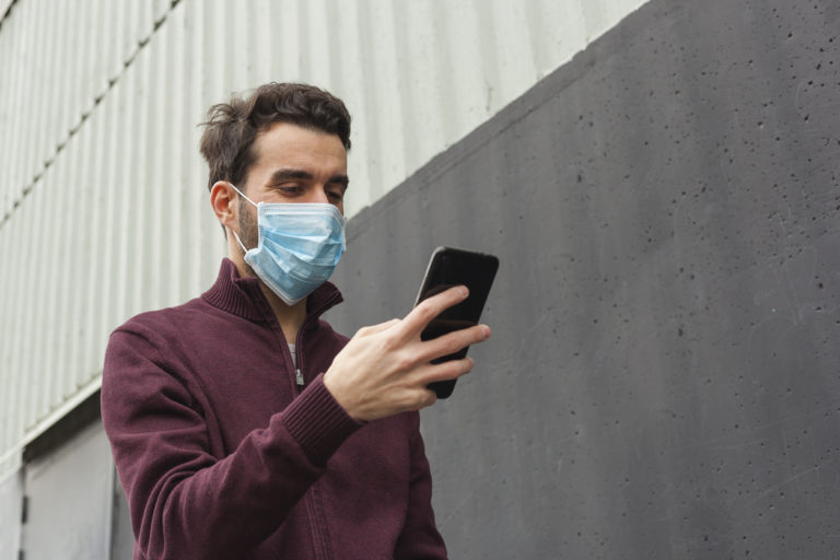 Bearded adult man using smartphone while wearing surgical mask