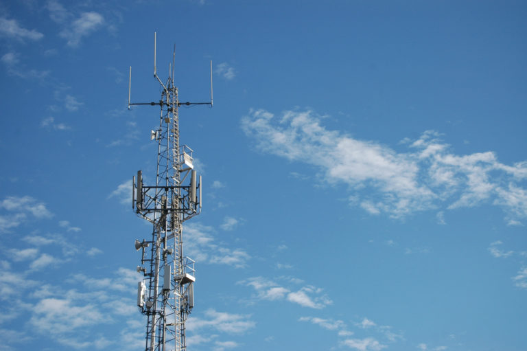 A Telecommunications tower against blue spring sky with a few wispy white clouds