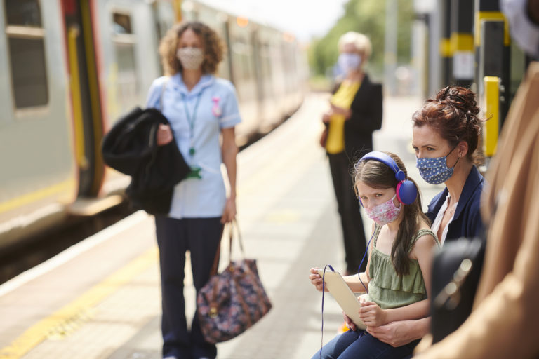 Image of girl and mother sitting on train platform in masks