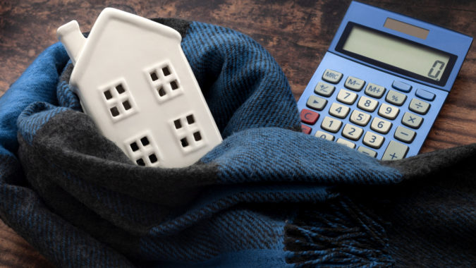 Warming efficiency of a residence and calculate heating costs concept with digital calculator, small house wrapped in warm wool neck scarf on wood background