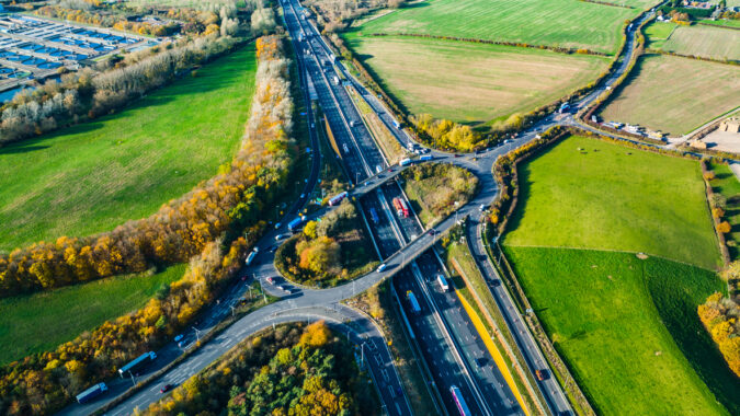 A modern bridge over a dual carriageway cutting through British farmland